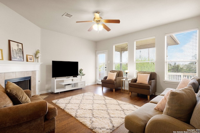 living area featuring a ceiling fan, visible vents, wood finished floors, a tile fireplace, and baseboards