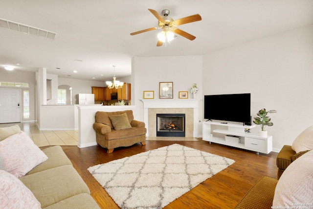 living area featuring ceiling fan with notable chandelier, a fireplace, visible vents, wood finished floors, and baseboards