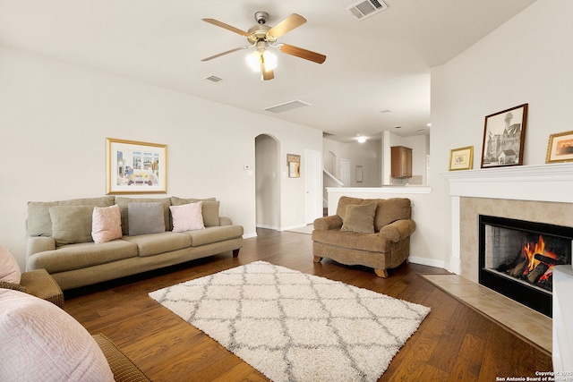 living area featuring dark wood-style floors, a ceiling fan, visible vents, arched walkways, and a tile fireplace