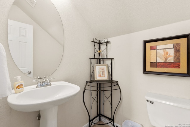bathroom featuring toilet, visible vents, a sink, and vaulted ceiling