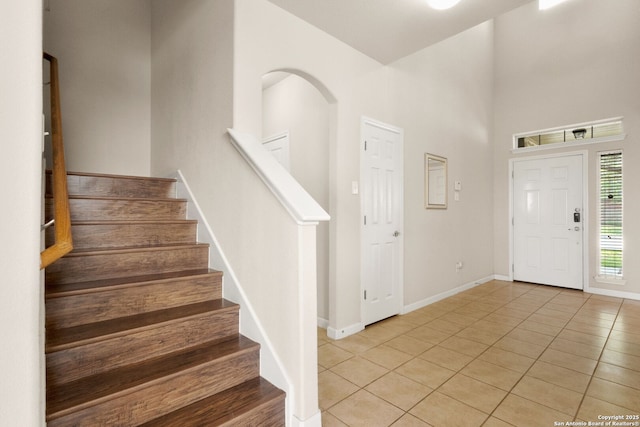 foyer with a towering ceiling, light tile patterned flooring, baseboards, and stairway