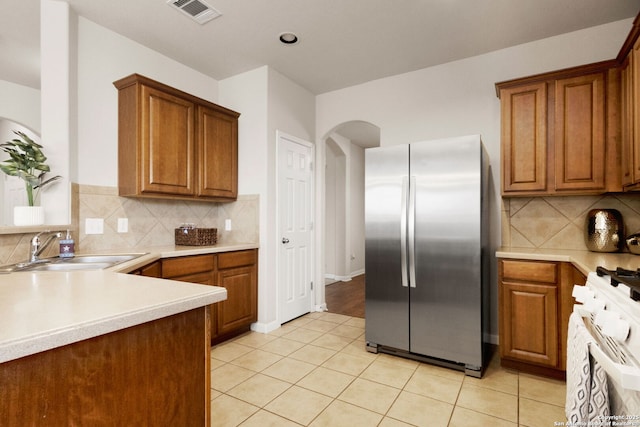 kitchen featuring white gas range oven, stainless steel refrigerator, visible vents, arched walkways, and a sink