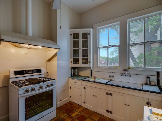 kitchen featuring tile counters, white gas range oven, white cabinets, and extractor fan