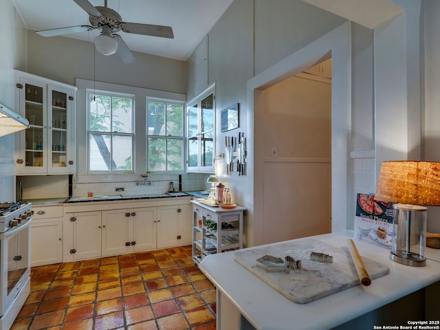 kitchen featuring gas stove, white cabinetry, a ceiling fan, decorative backsplash, and glass insert cabinets