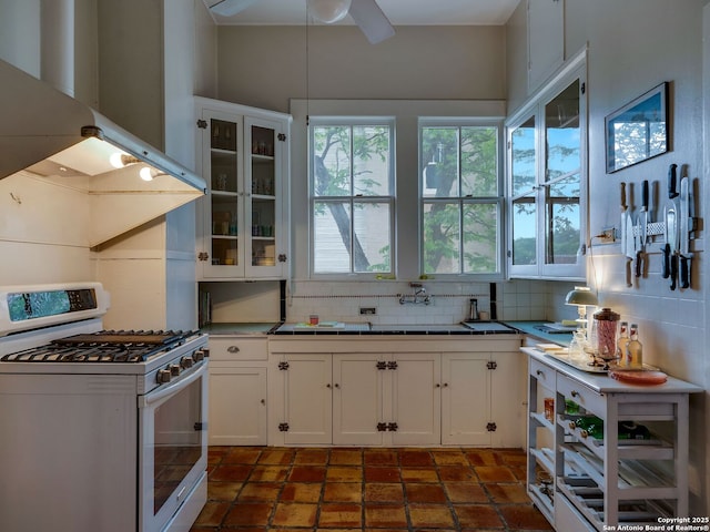 kitchen featuring white gas range, decorative backsplash, range hood, and white cabinetry