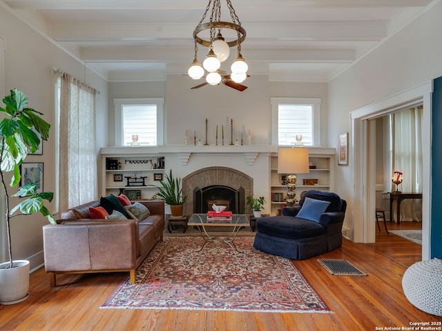 living area featuring a brick fireplace, beamed ceiling, visible vents, and wood finished floors