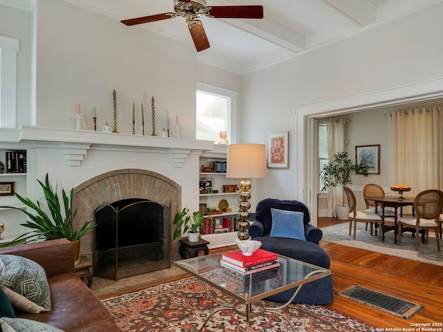 living room featuring ceiling fan, beam ceiling, a fireplace, wood finished floors, and visible vents