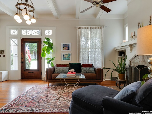 living area with a ceiling fan, a brick fireplace, wood finished floors, beamed ceiling, and ornamental molding