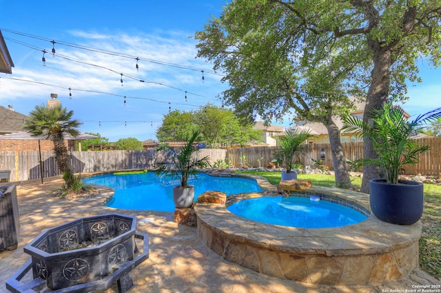 view of swimming pool featuring a patio, a fenced backyard, a pool with connected hot tub, and a fire pit