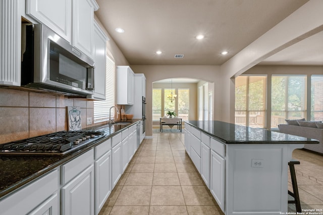 kitchen featuring a kitchen island, decorative backsplash, stainless steel appliances, arched walkways, and a sink