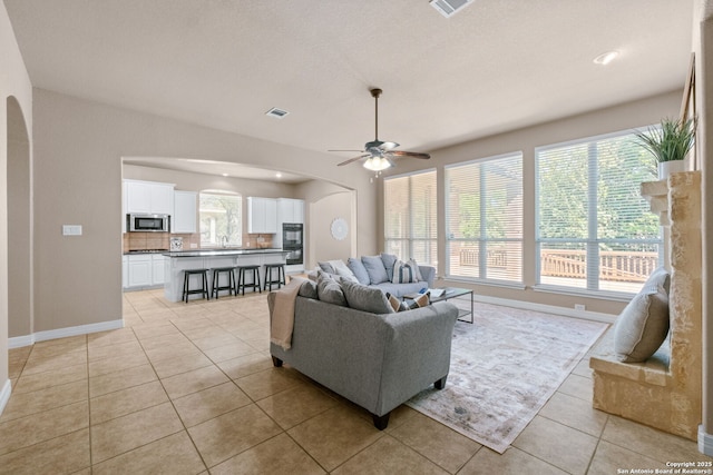 living area featuring arched walkways, ceiling fan, plenty of natural light, and light tile patterned floors