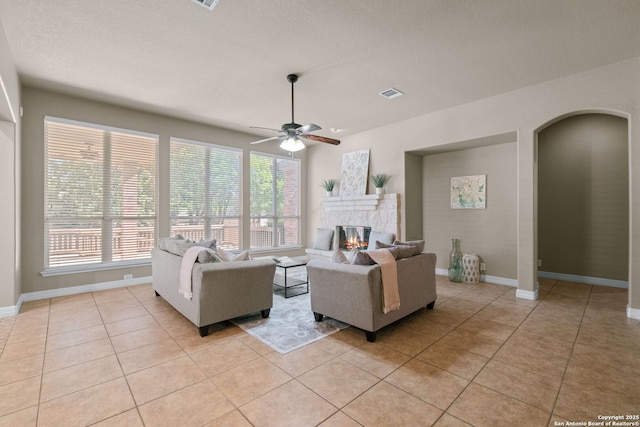 living room with visible vents, arched walkways, a ceiling fan, light tile patterned flooring, and a glass covered fireplace