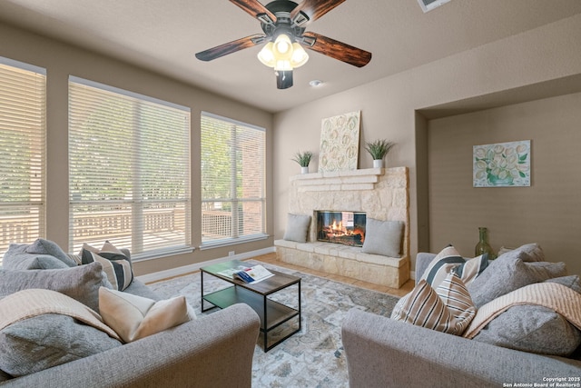 living area with a glass covered fireplace, baseboards, and a ceiling fan