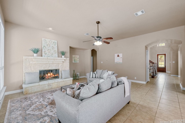 living room with light tile patterned floors, arched walkways, a ceiling fan, a glass covered fireplace, and visible vents