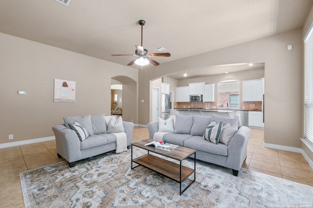 living room with arched walkways, light tile patterned floors, baseboards, and a ceiling fan