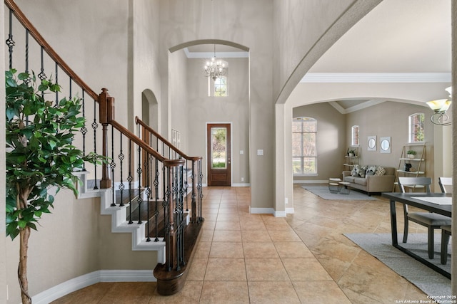 entryway featuring a notable chandelier, baseboards, ornamental molding, stairway, and arched walkways