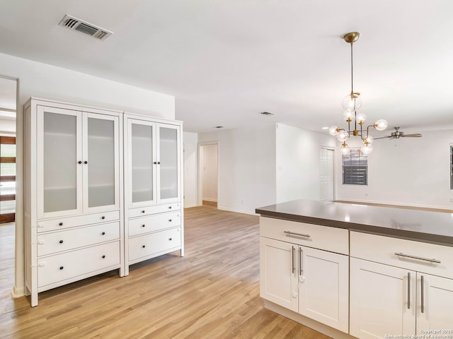 kitchen with white cabinetry, dark countertops, visible vents, light wood finished floors, and hanging light fixtures