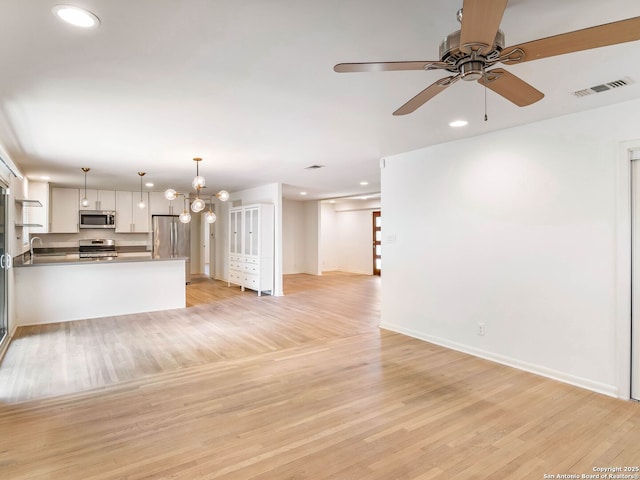 unfurnished living room featuring ceiling fan with notable chandelier, visible vents, recessed lighting, a sink, and light wood finished floors