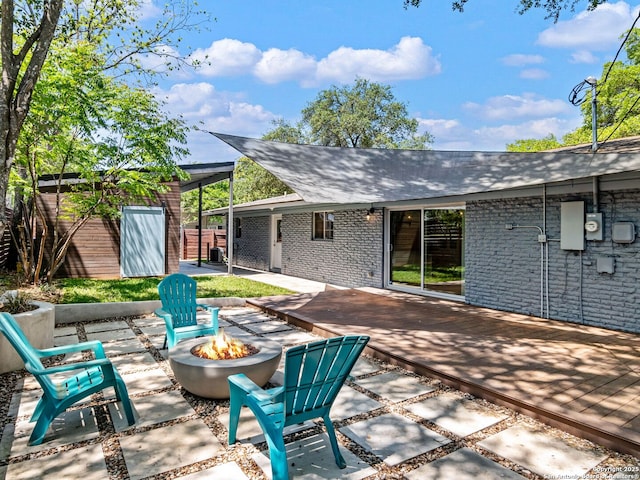view of patio featuring an outbuilding, a deck, fence, and an outdoor fire pit