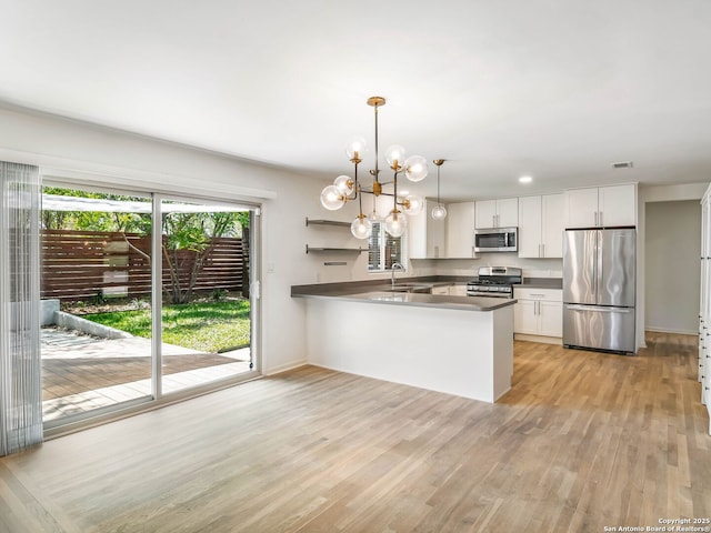 kitchen with a sink, light wood-type flooring, a peninsula, white cabinetry, and stainless steel appliances