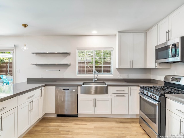 kitchen with white cabinets, a sink, dark countertops, stainless steel appliances, and light wood-style flooring