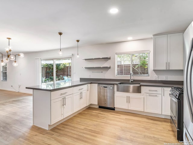 kitchen with a peninsula, light wood-style flooring, dark countertops, stainless steel appliances, and a sink