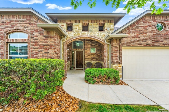 doorway to property featuring an attached garage, concrete driveway, and brick siding