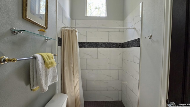 bathroom featuring a textured wall, tiled shower, and toilet