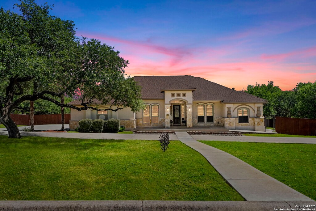 9102 Portofino, San Antonio, TX 78266 - view of front of house with stucco siding, a yard, stone siding, and fence