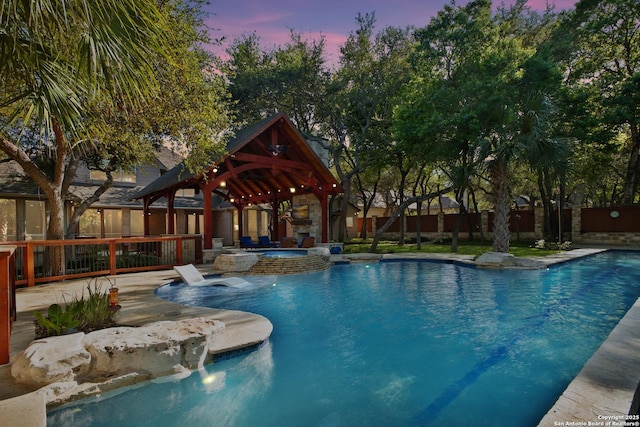 pool at dusk featuring fence, a gazebo, and a pool with connected hot tub
