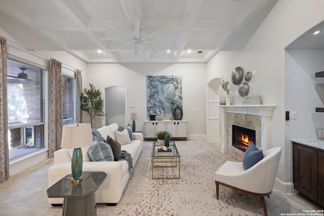 living area with arched walkways, a tiled fireplace, a ceiling fan, beamed ceiling, and coffered ceiling