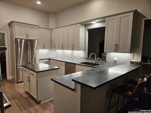 kitchen featuring a kitchen island, dark wood-style flooring, a sink, dark countertops, and stainless steel appliances