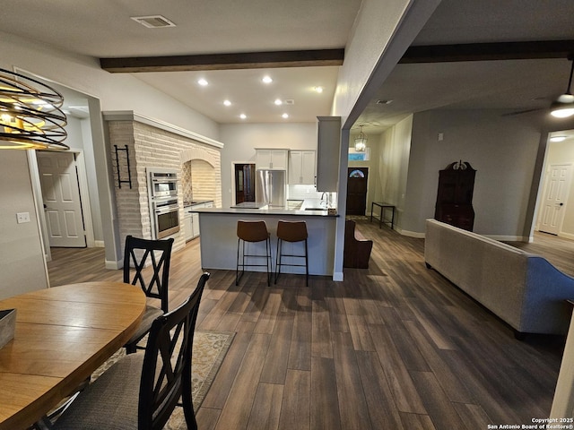 kitchen with white cabinets, dark wood-style flooring, appliances with stainless steel finishes, a kitchen bar, and beamed ceiling