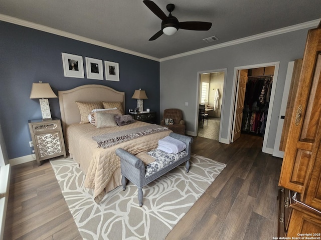 bedroom with wood finished floors, baseboards, ornamental molding, and a walk in closet