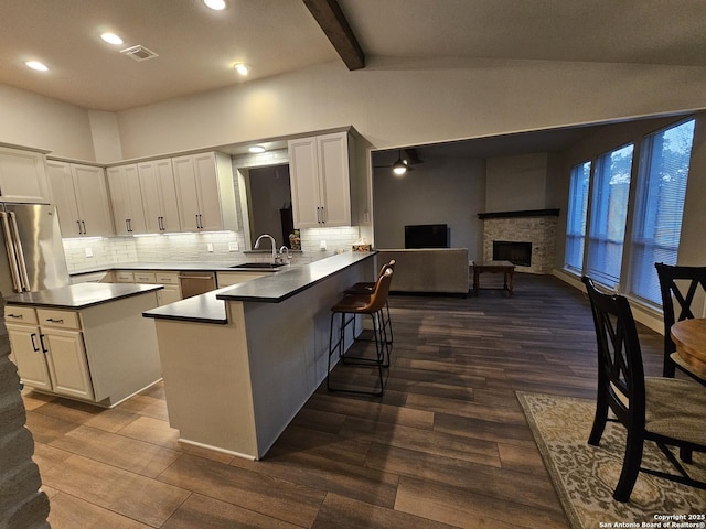 kitchen featuring a kitchen breakfast bar, a peninsula, dark countertops, visible vents, and vaulted ceiling with beams