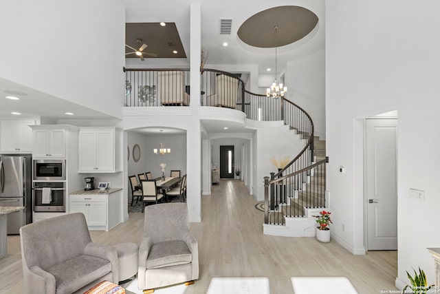 living area featuring stairway, light wood finished floors, a high ceiling, visible vents, and recessed lighting