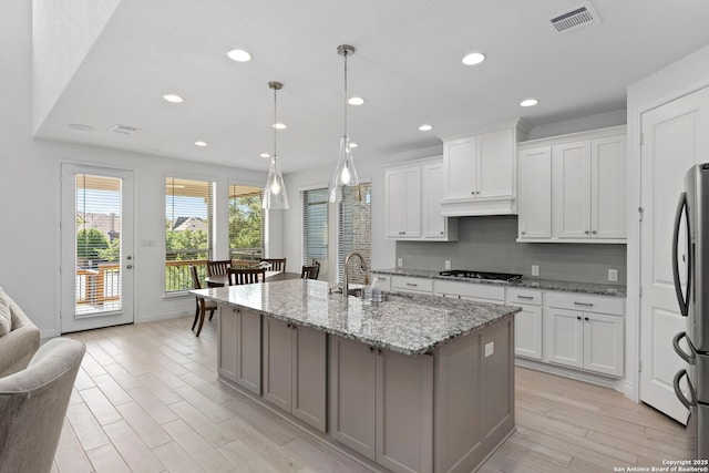 kitchen featuring tasteful backsplash, a sink, light wood finished floors, visible vents, and freestanding refrigerator