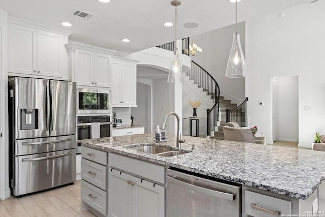 kitchen with an island with sink, stainless steel appliances, visible vents, a sink, and white cabinetry