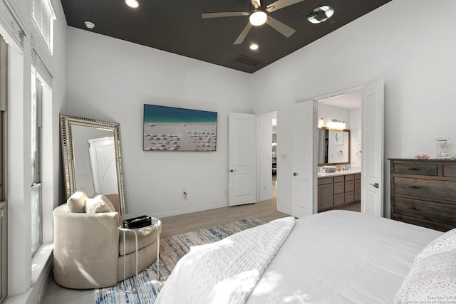 bedroom featuring baseboards, visible vents, wood finished floors, a high ceiling, and ensuite bath