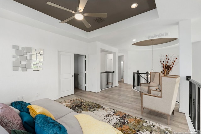 living room with baseboards, wood finished floors, visible vents, and a raised ceiling