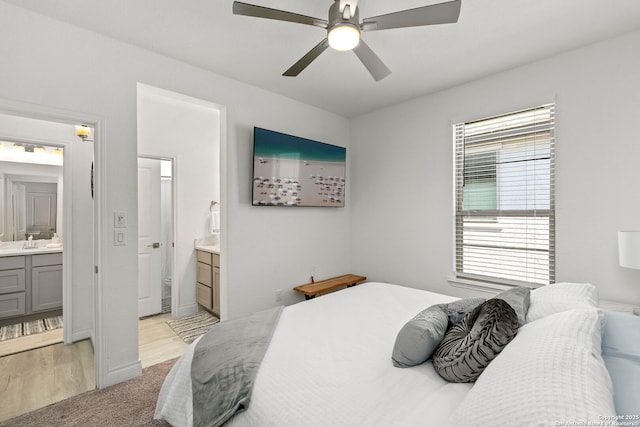 bedroom featuring light wood finished floors, ensuite bath, light carpet, and ceiling fan