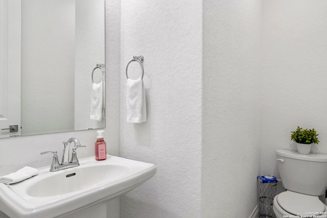 bathroom featuring a textured wall, toilet, and a sink