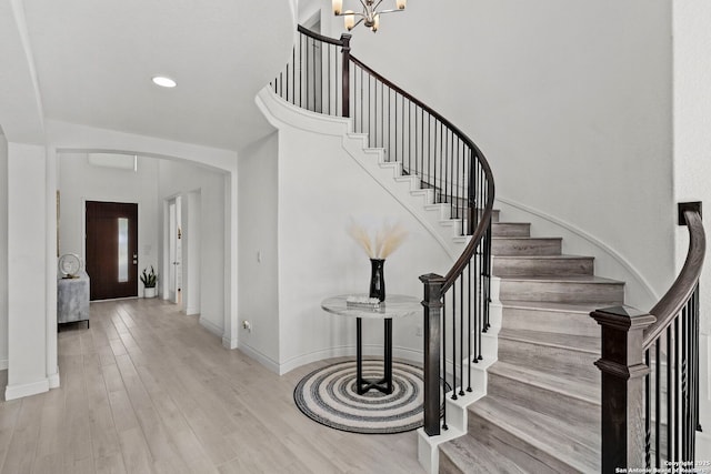 staircase with baseboards, wood finished floors, arched walkways, and a chandelier