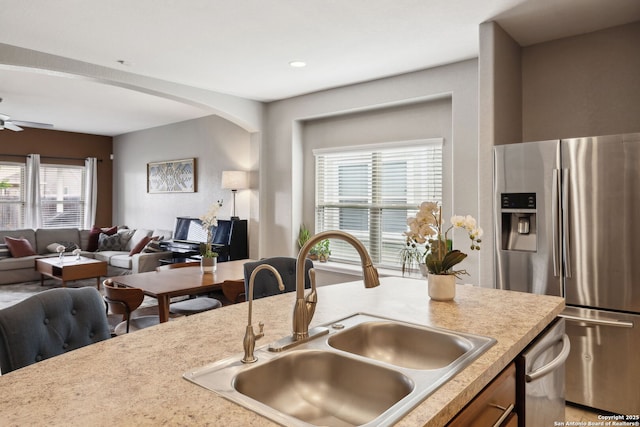 kitchen with stainless steel fridge with ice dispenser, arched walkways, a sink, open floor plan, and light countertops