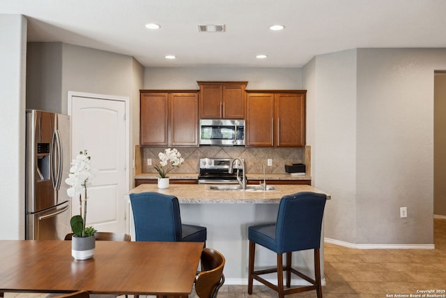 kitchen featuring visible vents, a sink, brown cabinetry, stainless steel appliances, and backsplash