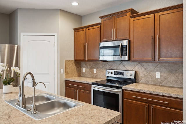 kitchen with appliances with stainless steel finishes, light countertops, a sink, brown cabinets, and decorative backsplash