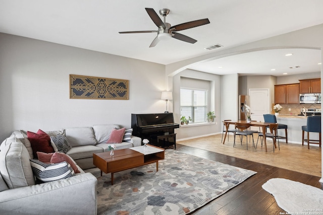living area with dark wood-type flooring, arched walkways, a ceiling fan, visible vents, and baseboards