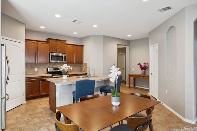 kitchen with an island with sink, backsplash, visible vents, appliances with stainless steel finishes, and a sink