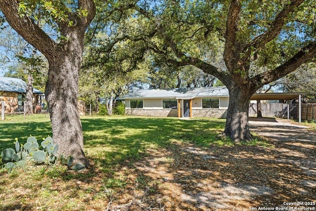 view of front of property featuring a carport, a front lawn, fence, and stone siding