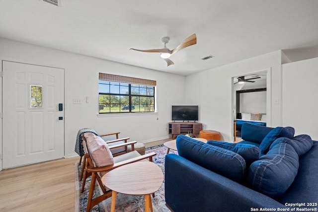 living area featuring light wood-style floors, visible vents, baseboards, and ceiling fan